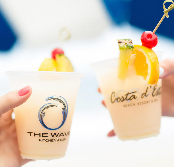 Two people holding alcoholic drinks in Coste d' Este and The Wave Kitchen branded cups